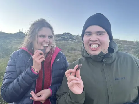 Tvö hlæjandi, vel klædd útí í náttúrunni að borða súkkulaði kex