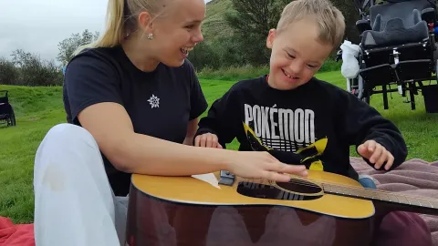 Kona og barn sitja í grasi og spila á gítar