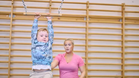 Boy holding a swing and woman pushing in background